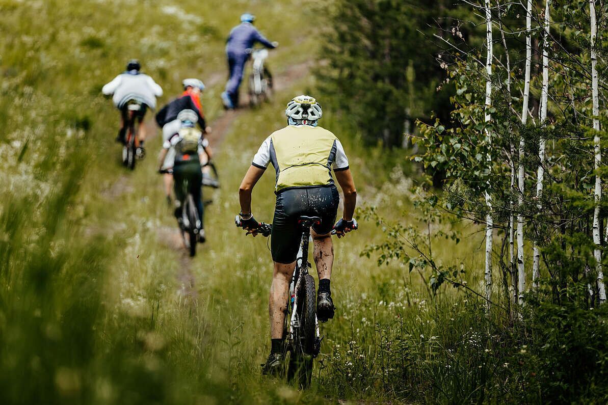 Un grupo de ciclistas de montaña en un sendero estrecho rodeado de vegetación.