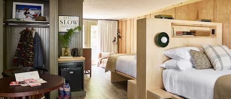 Une chambre d’hôtel de taille réduite, comprenant un lit, un petit bureau, une chaise, une table et une kitchenette.
