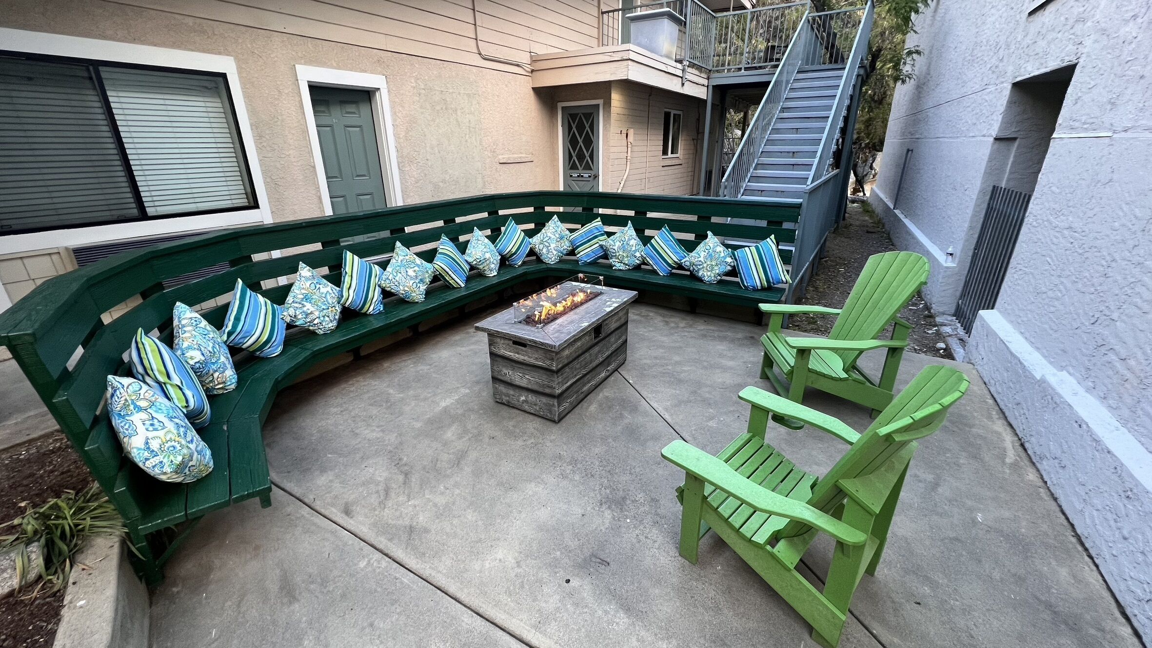 A green outdoor seating area with a fire pit, a bench, and a chair.