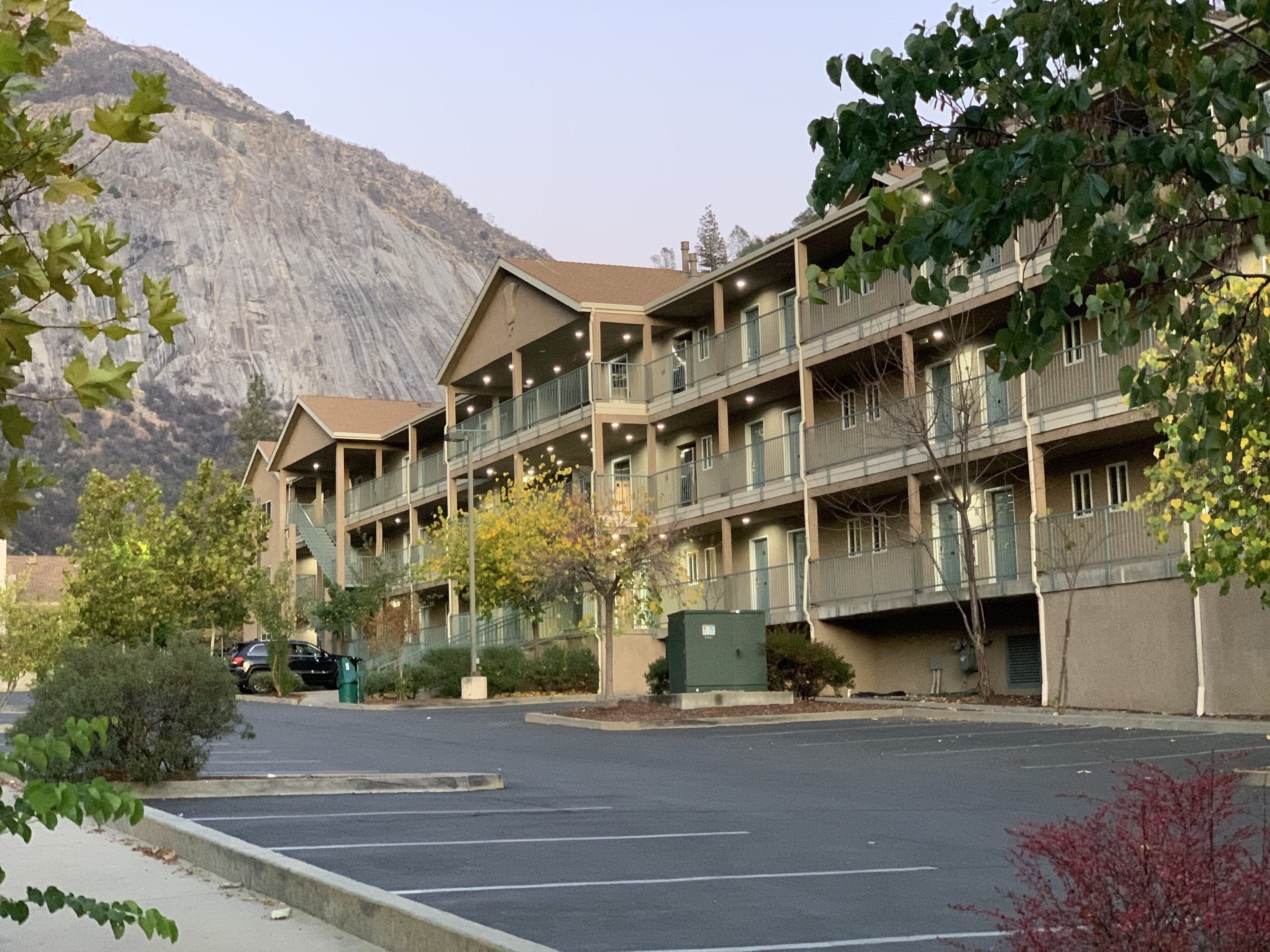 A multi-story hotel with balconies, a parking lot, and a mountain in the background.