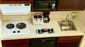 Una cucina compatta con fornello, forno a microonde, tostapane, macchina del caffè e lavello.