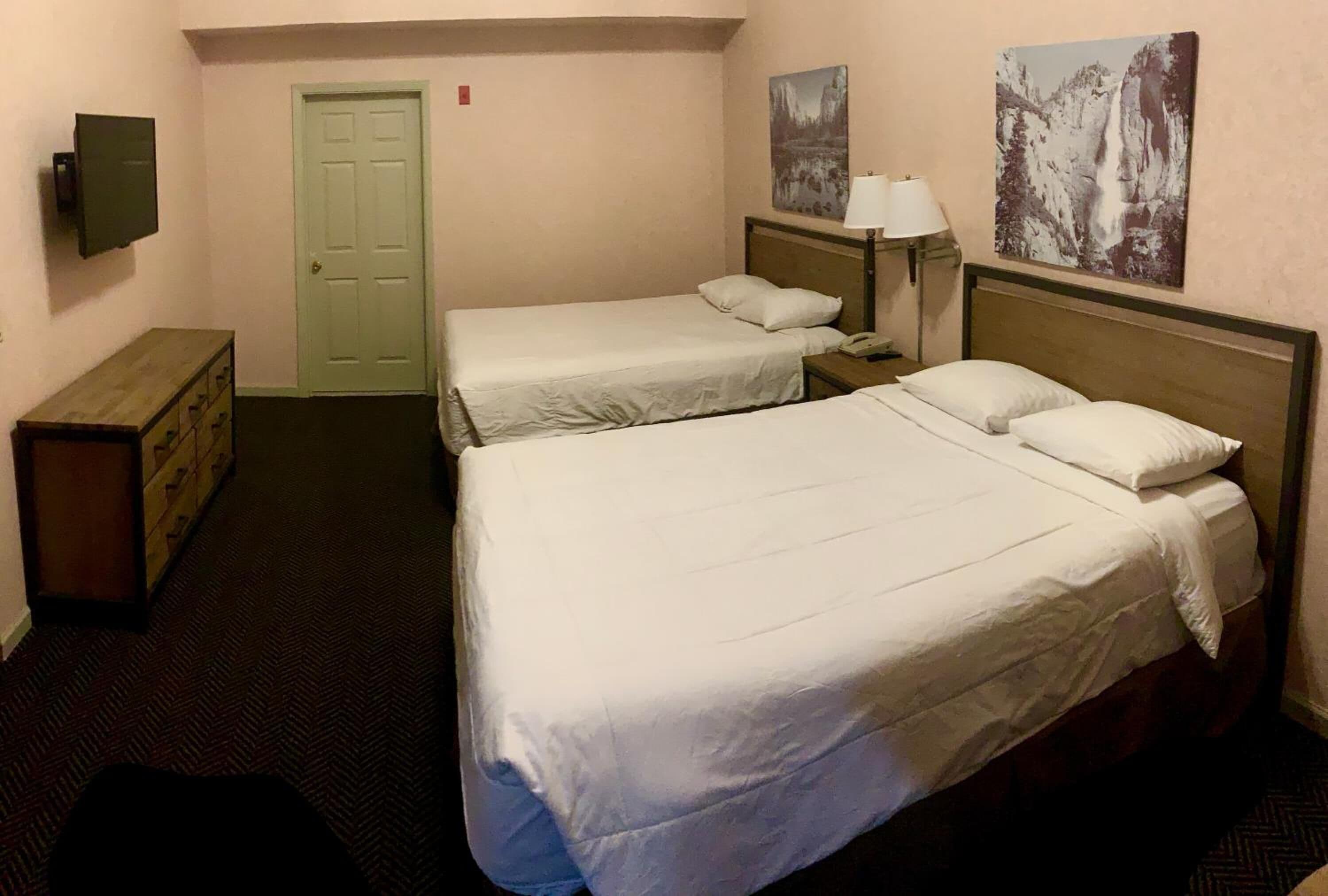 Une chambre d’hôtel avec deux lits, une commode en bois, une télévision et des œuvres d’art accrochées aux murs.