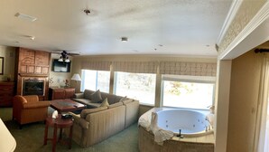 A living room with a sofa, a coffee table, a fireplace, a television, and a large window with blinds. - Yosemite View Lodge (El Portal)