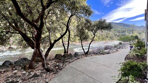 A concrete pathway alongside a river with trees and rocks.
