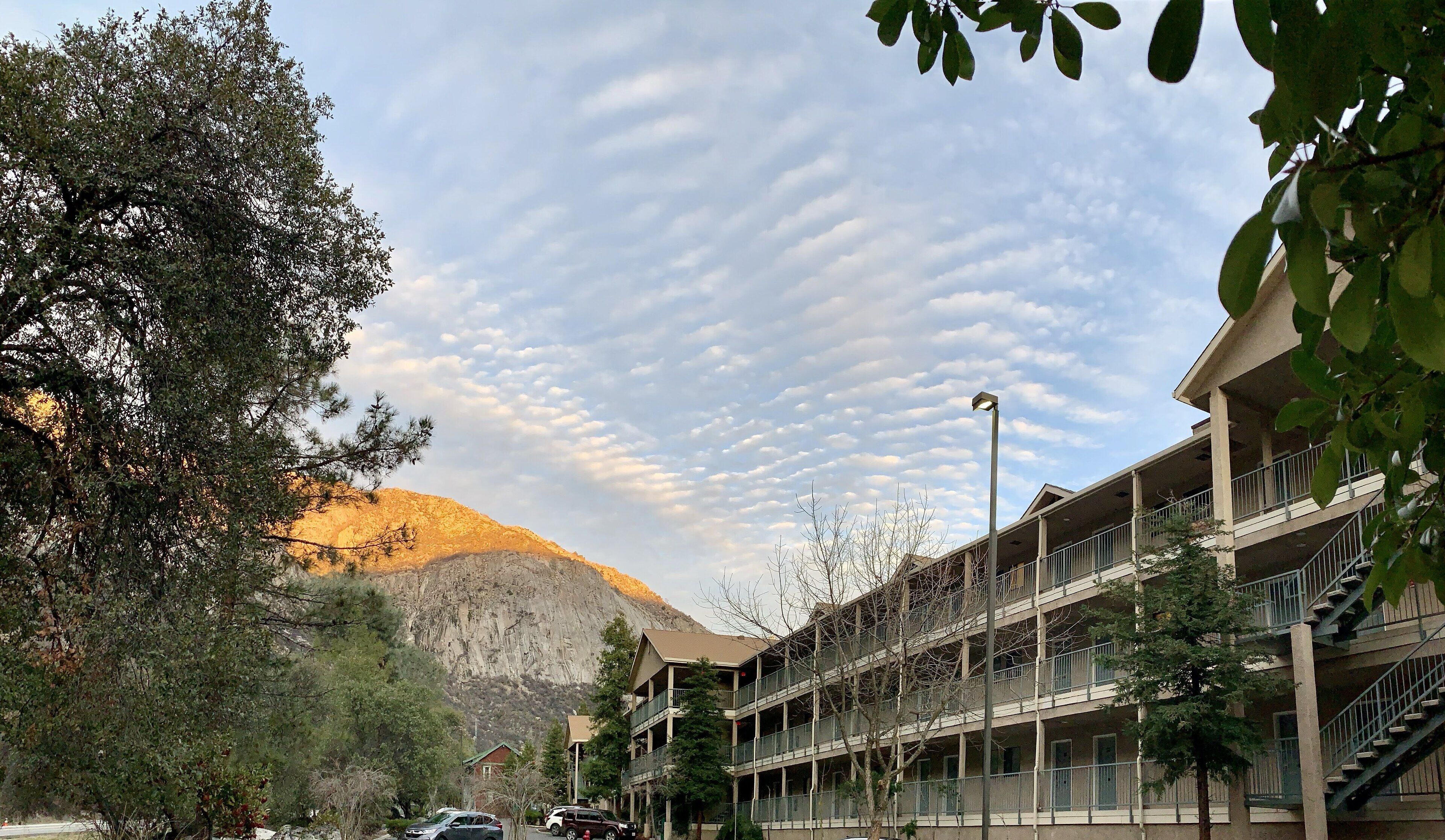 A multi-story building with balconies, a mountain in the background, and a clear sky with cloud formations.