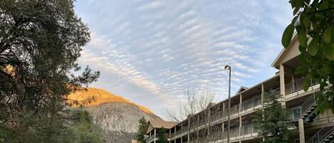 Un edificio de varios pisos con balcones, una montaña al fondo y un cielo despejado con formaciones de nubes.
