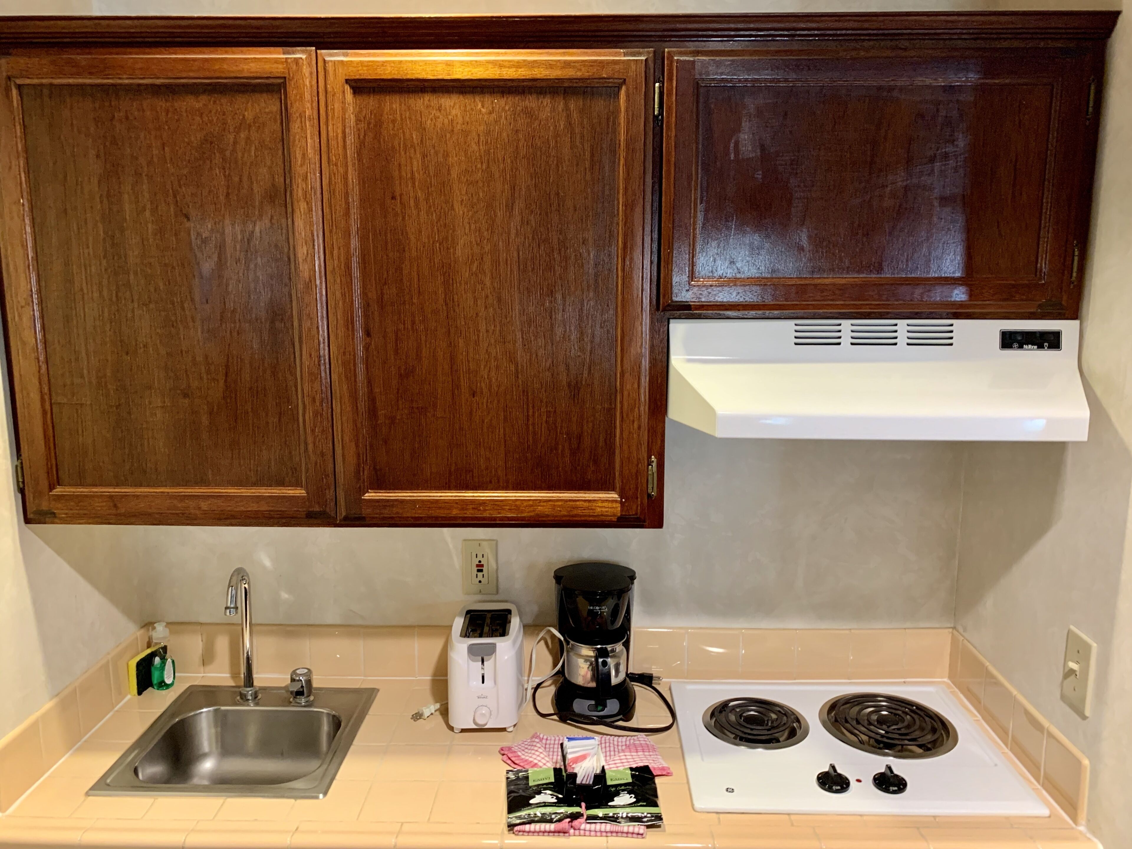 A kitchen with wooden cabinets, a stainless steel sink, a white toaster, a black coffee maker, and a white stove.