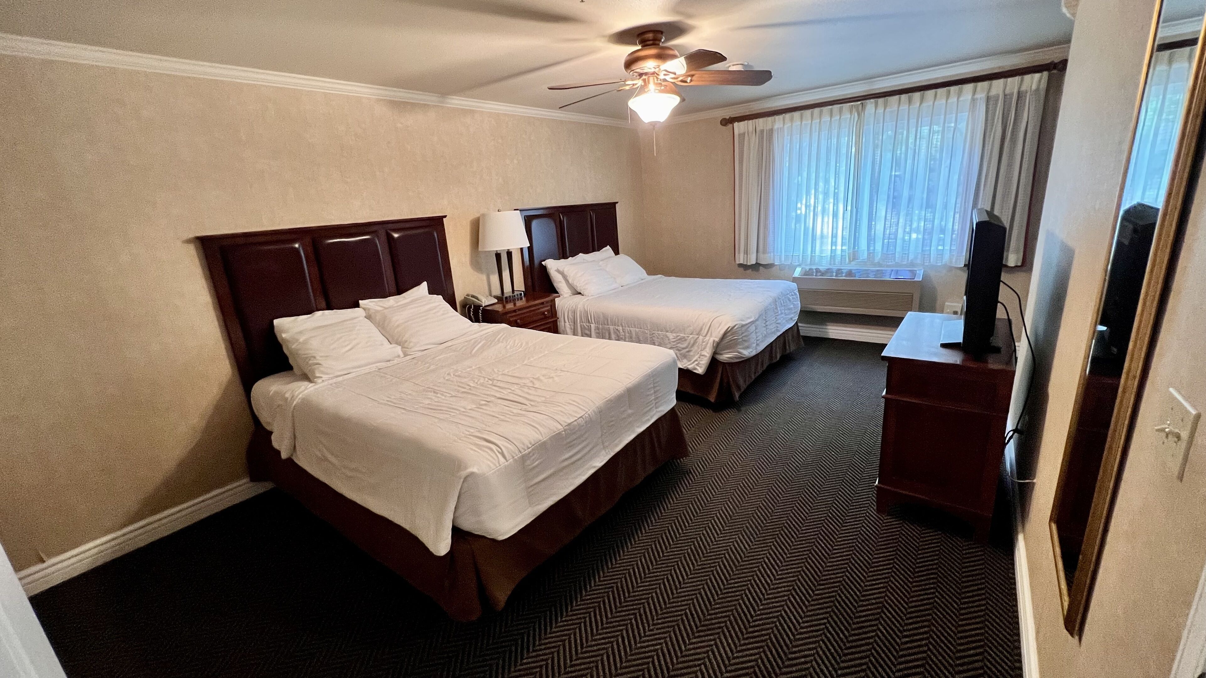 Een hotelkamer met twee bedden, een plafondventilator, een televisie en een raam met gordijnen.