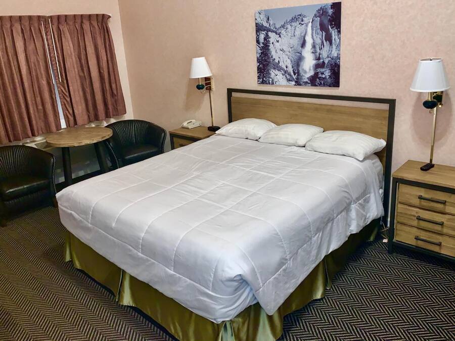 A hotel room with a large bed, a desk with a chair, two bedside lamps, a telephone, and a painting on the wall.