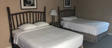 Une chambre d’hôtel avec deux lits simples, une table de chevet avec une lampe et deux tableaux encadrés au mur.