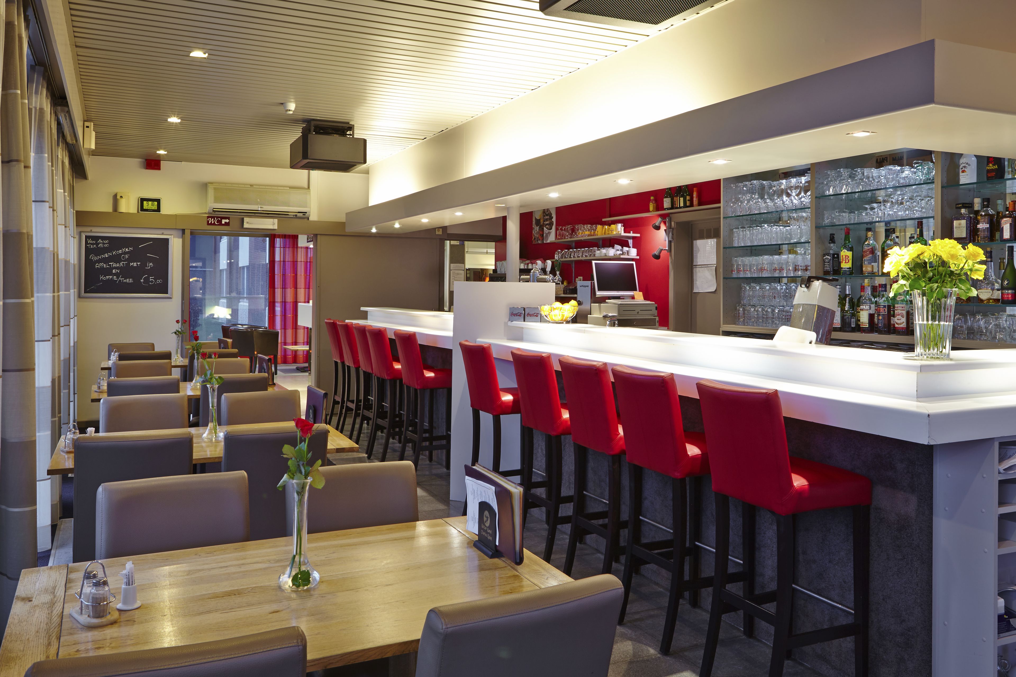 A modern restaurant with a bar area, red bar stools, and a variety of seating options.