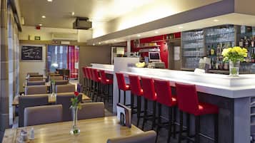 A modern restaurant with a bar area, red bar stools, and a variety of seating options.