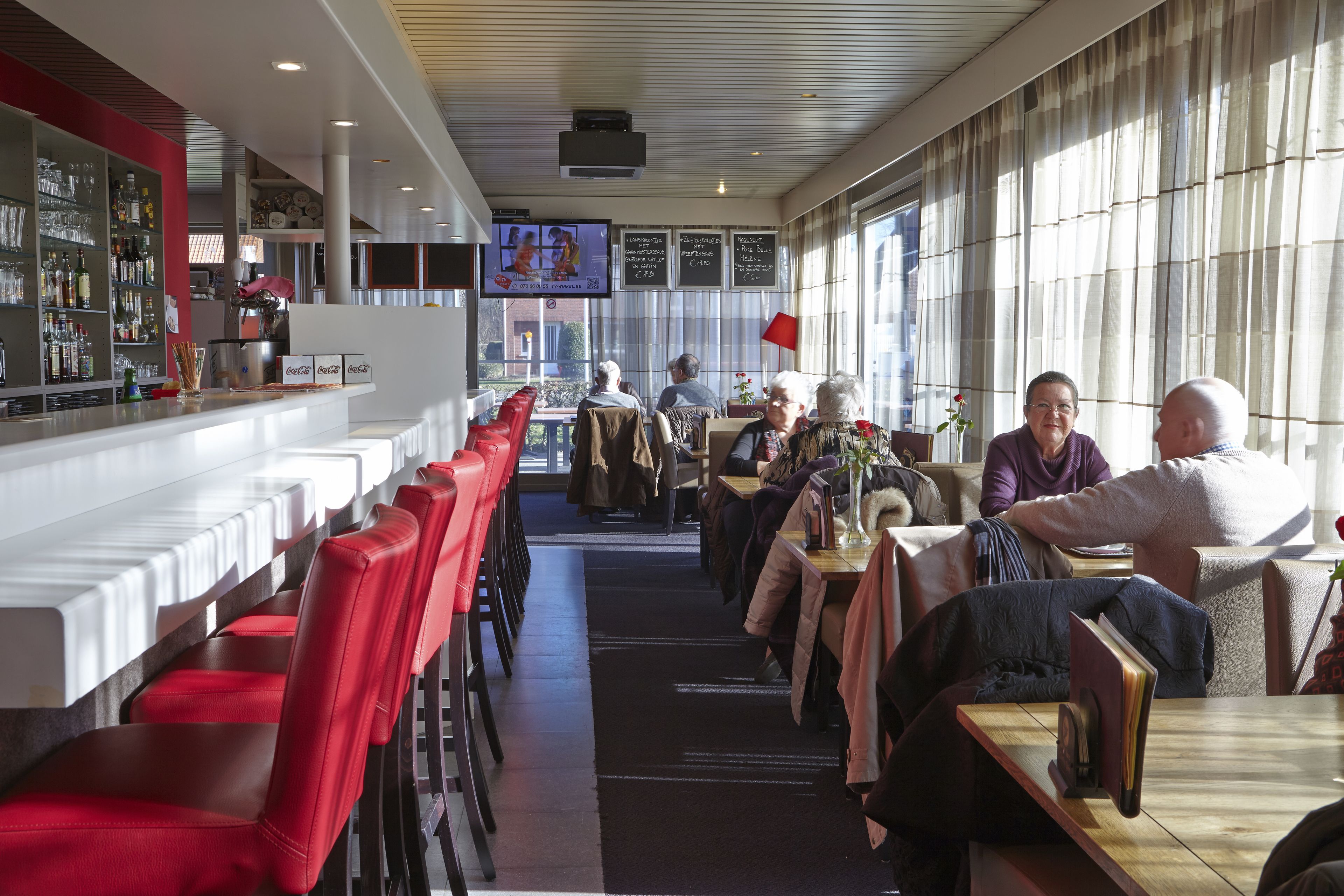 Un restaurante con sillas rojas, una zona de bar y una pantalla de televisión.