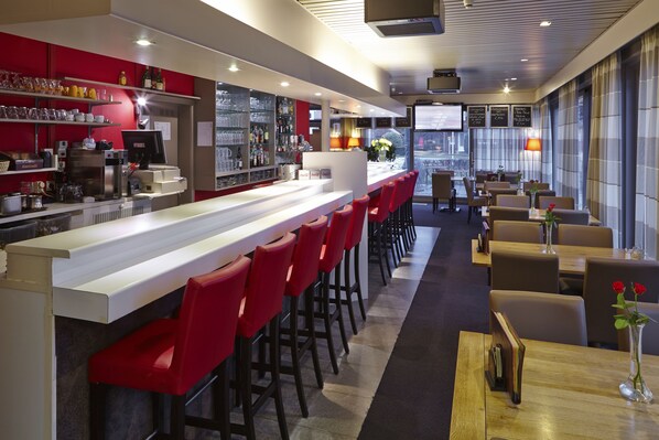 A modern bar area with a long counter, red bar stools, and a seating area with tables and chairs.