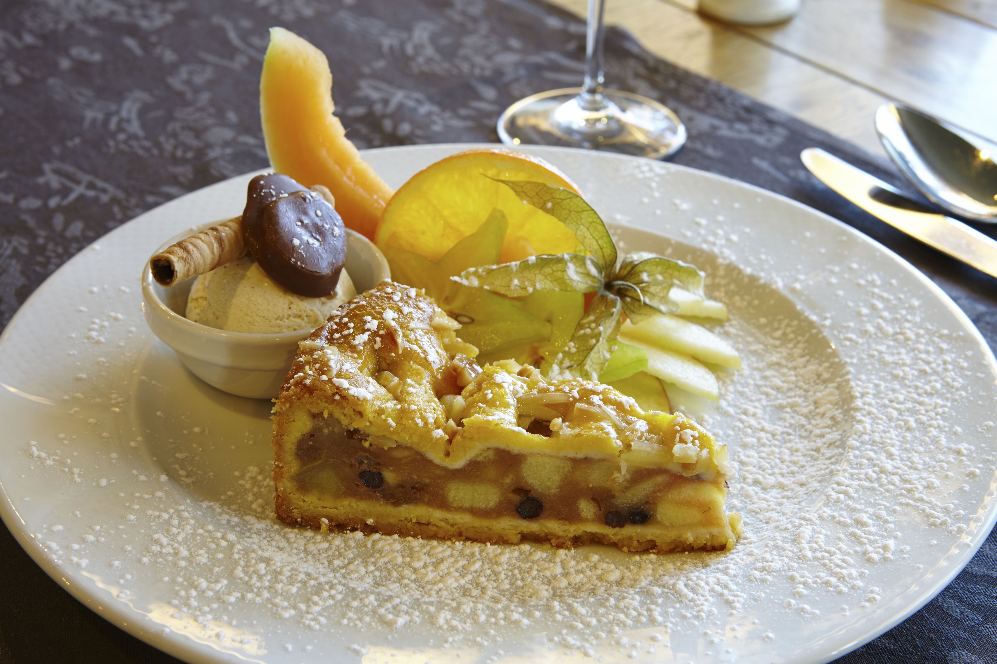 Un plato de postre con una porción de tarta de manzana, una bola de helado y una guarnición de fruta.
