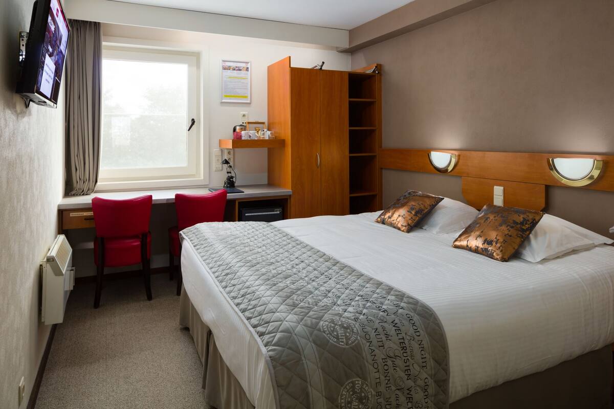 A hotel room with a bed, a desk, a chair, a wardrobe, and a window.