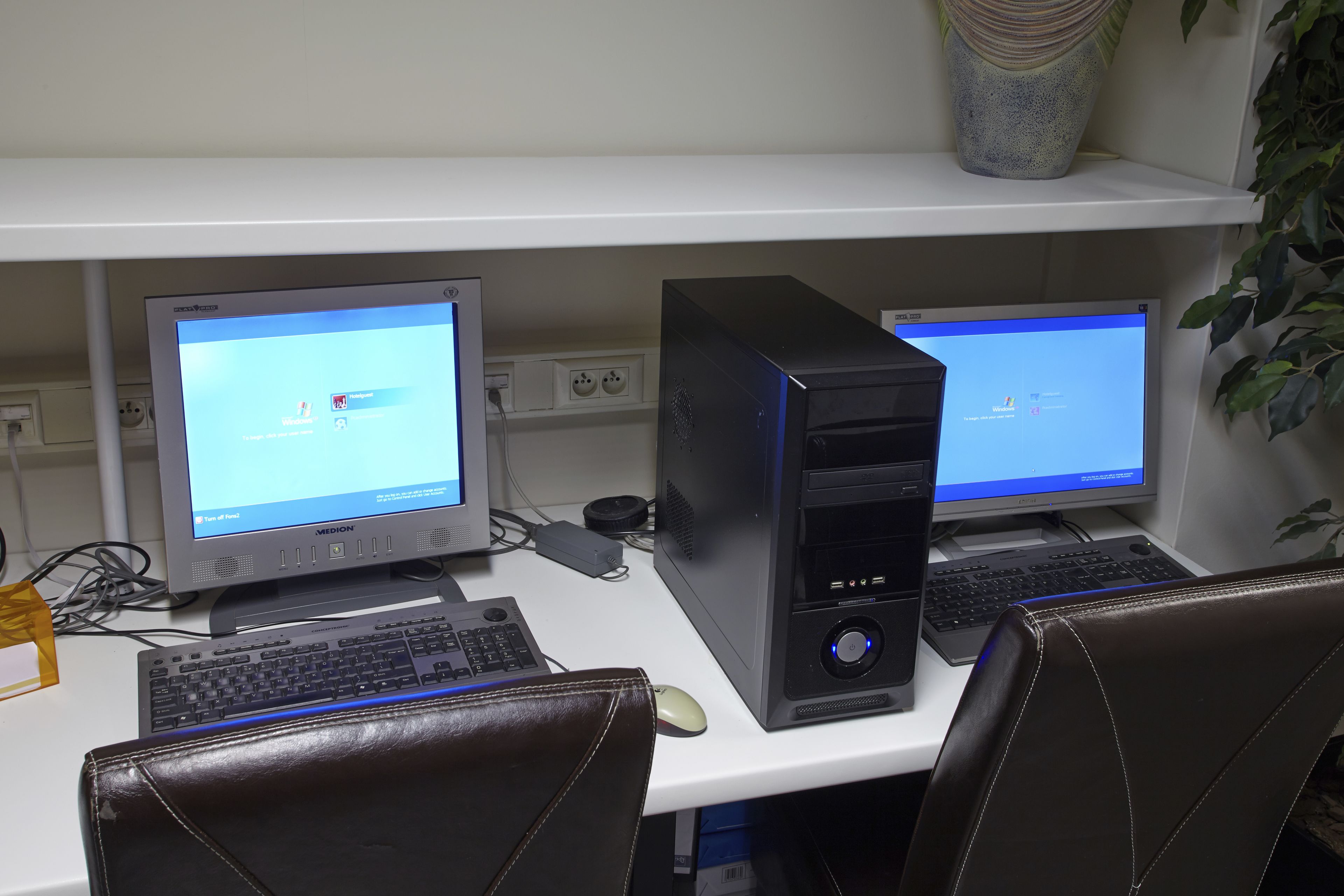 A workspace with two desktop computers, a keyboard, a mouse, and leather chairs.