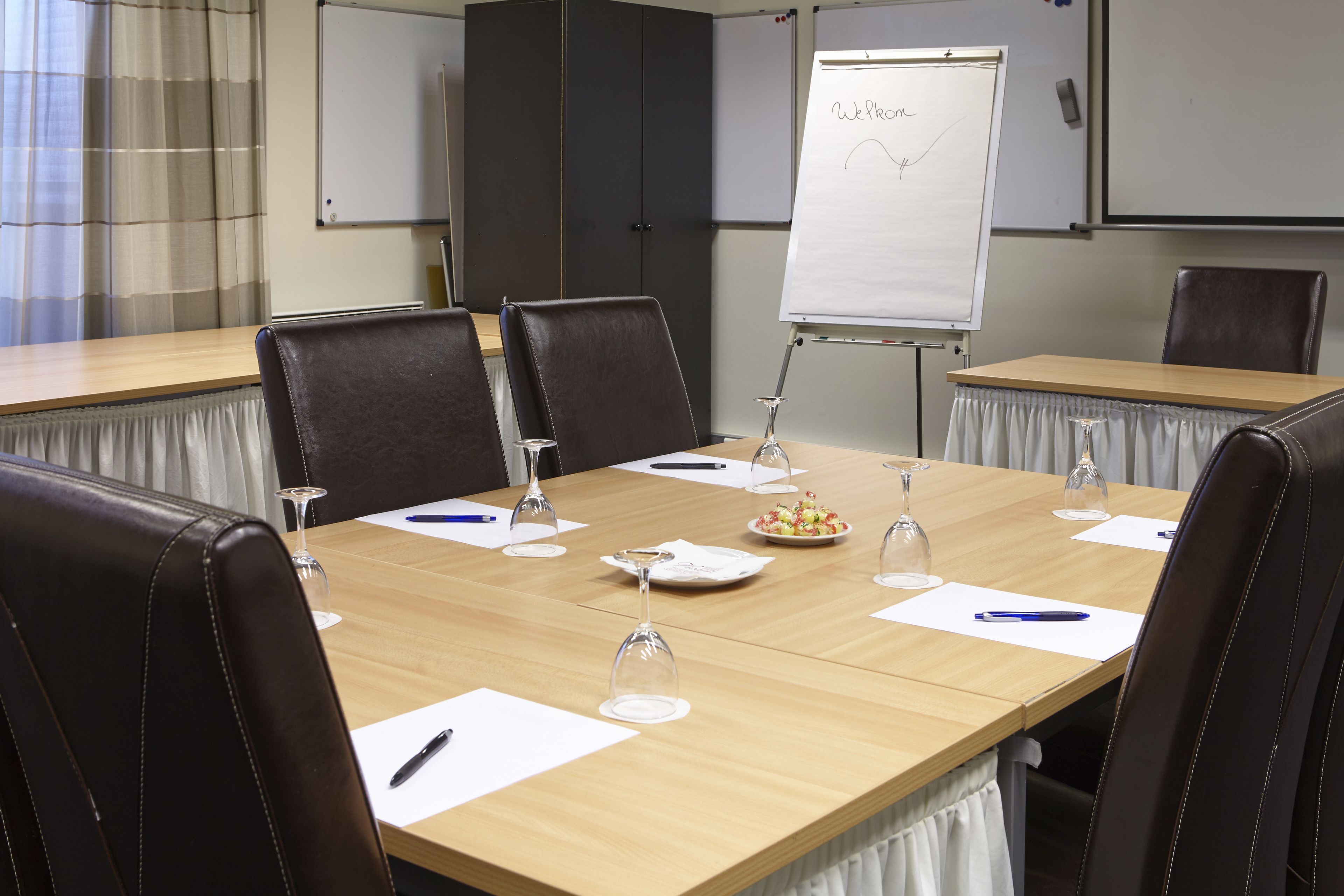 A conference room with a long table, chairs, a whiteboard, and a whiteboard with 'Welcome' written on it.