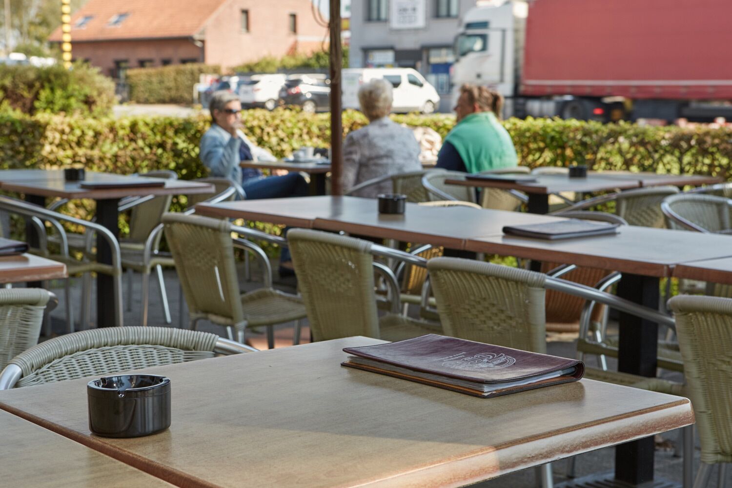 Un café en plein air avec des chaises et des tables en osier, un cendrier noir et un livre posé sur une table.