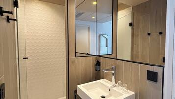 Une salle de bain moderne avec une douche à parois de verre, un lavabo blanc et un grand miroir.