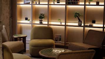 A cozy seating area with wicker chairs and a small table, a bookshelf with various items, and a wall with a textured pattern.