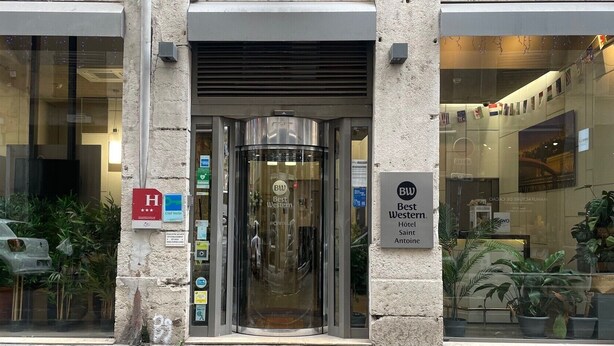 La entrada del Best Western Hôtel Saint Antoine, con una puerta giratoria, un letrero de Best Western y una señal roja con la letra “H” que indica que es un hotel.