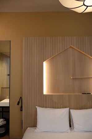 A hotel room with a bed, a nightstand, a mirror, and a wall-mounted light fixture.