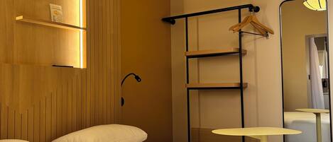 A hotel room with a bed, a bedside table, a hanging light fixture, a mirror, and a wooden panel wall.