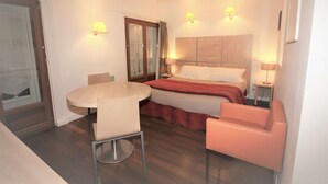 Una habitación de hotel con una cama, una mesa redonda con una silla, un pequeño sofá rosa y dos lámparas de noche.