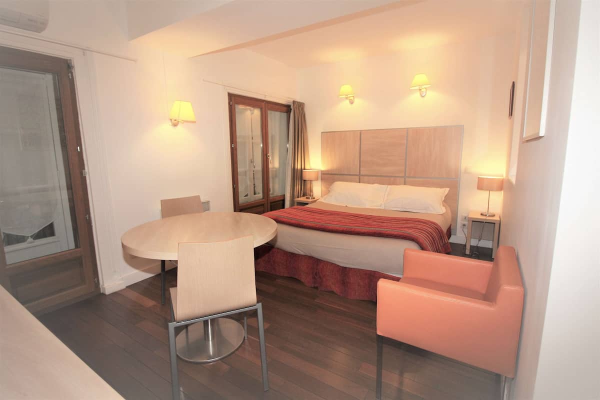 A hotel room with a bed, a round table with a chair, a small pink sofa, and two bedside lamps.