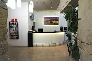 A reception area with a curved counter, a digital screen, a coffee machine, and a bookshelf with magazines. - Best Western Hotel Saint Antoine (Lyon)