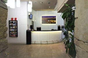 Un'area reception con un bancone curvo, uno schermo digitale, una macchina per caffè e una libreria con riviste.