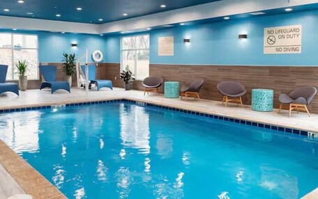An indoor swimming pool with blue water, surrounded by lounge chairs and a sign indicating no lifeguard on duty.