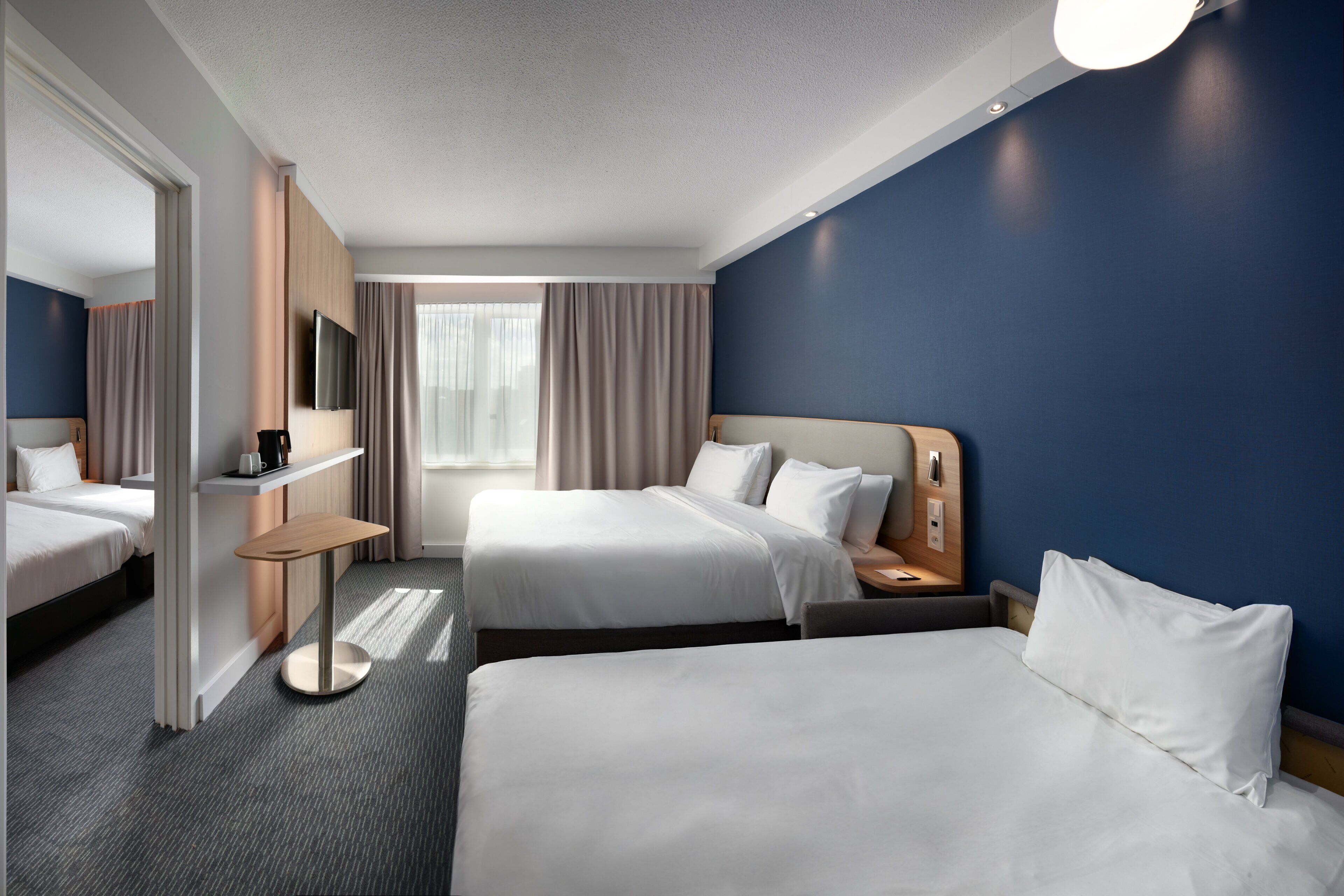 Habitación de hotel con dos camas, televisión, mesita de noche y ventana con cortinas.