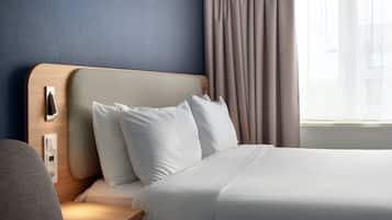 A hotel room with a neatly made bed, a bedside table, a nightstand, a lamp, and a window with curtains.