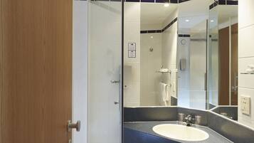 Ein modernes Badezimmer mit Duschkabine aus Glas, einem großen Spiegel und einem Waschbecken auf einer dunklen Ablagefläche.