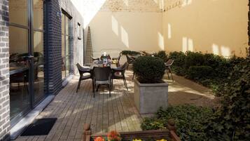 Un espace extérieur aménagé en patio, avec une table et des chaises, un pot de fleurs et un mur en briques.
