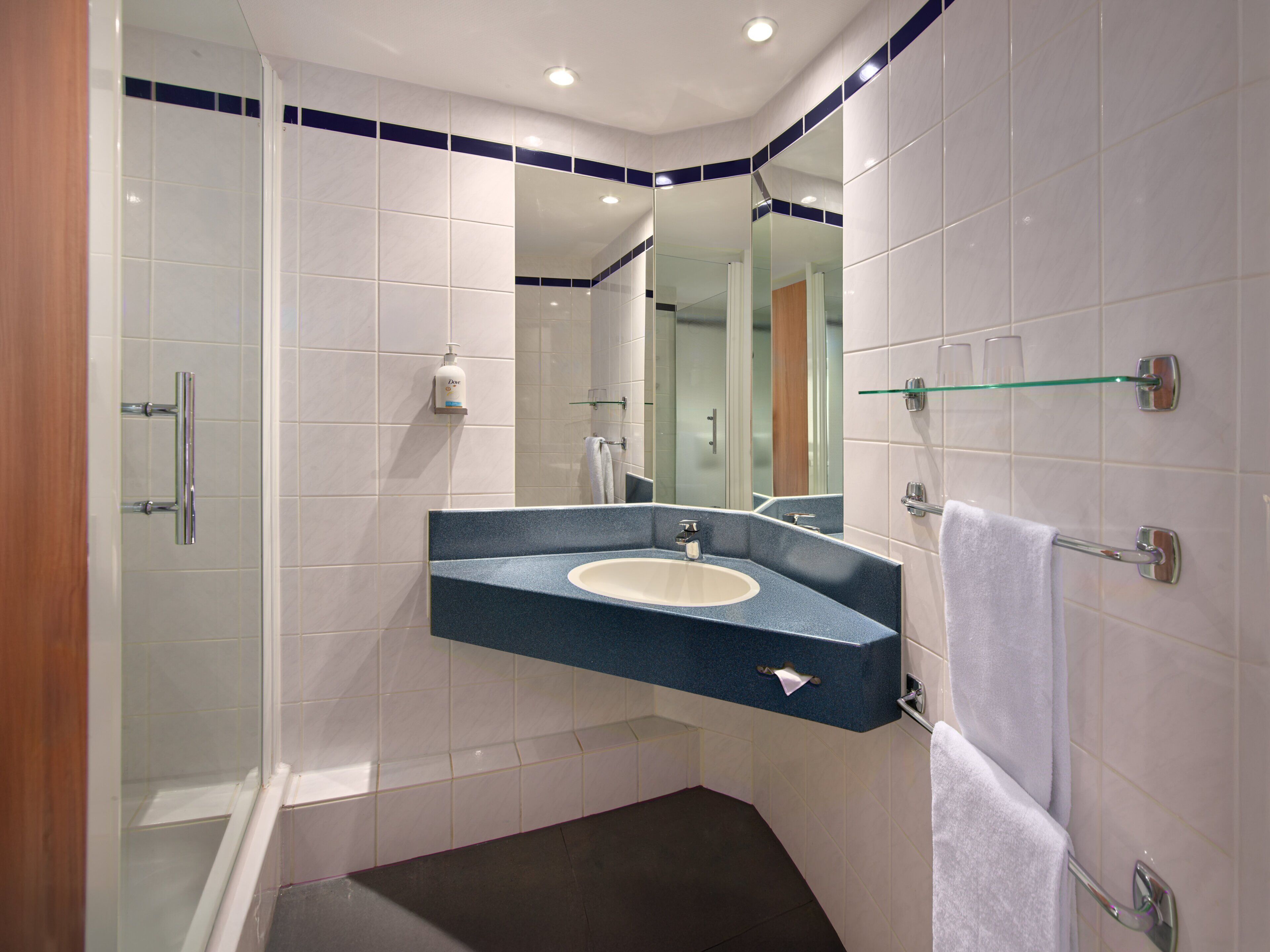A modern bathroom with a curved sink, a glass shower enclosure, and a mirror with a blue border.