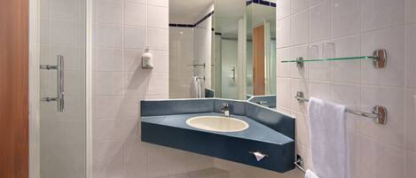 Un baño moderno con un lavamanos curvo, una cabina de ducha de vidrio y un espejo con borde azul.