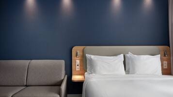 A hotel room with a bed, a sofa, and a wall with recessed lighting.