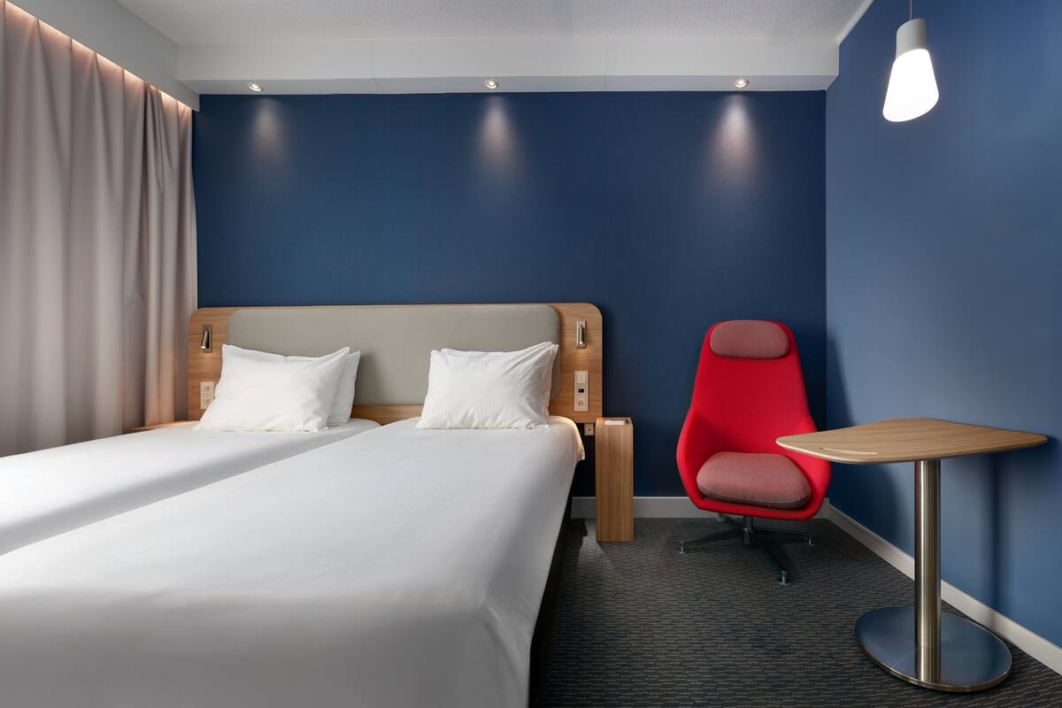 A hotel room with a bed, a red chair, and a small table.