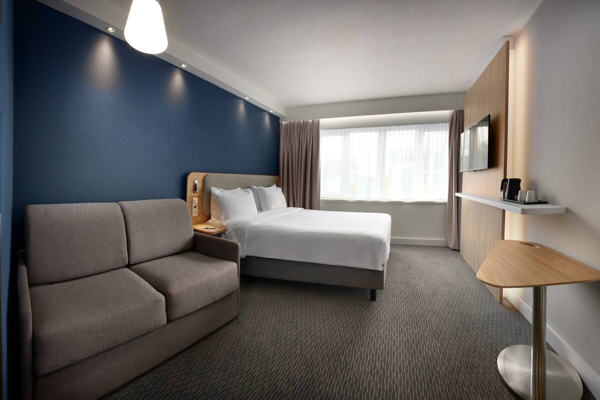 A modern hotel room with a bed, a sofa, a TV, and a coffee maker.