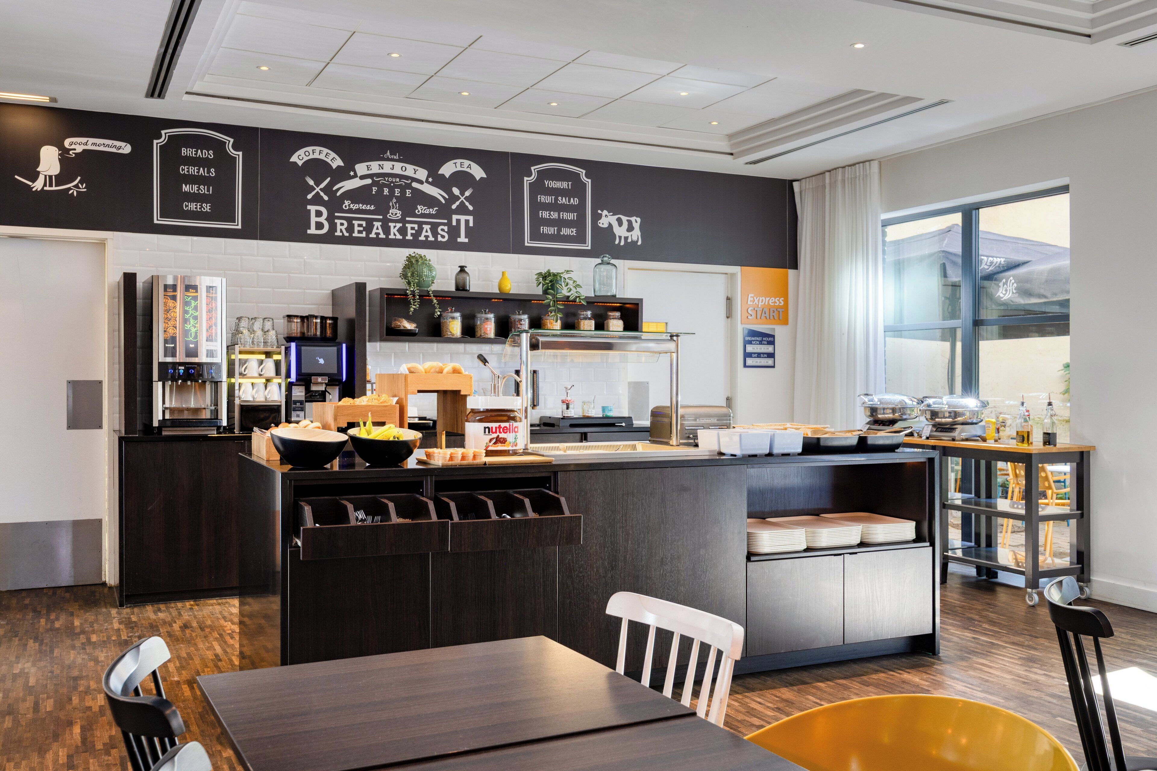 Un espace pour le petit-déjeuner comprenant un comptoir, des sièges et un panneau indiquant les heures du service.