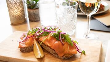 Un sandwich servi sur une planche en bois, accompagné d’un verre de vin blanc et d’une bougie en arrière-plan.