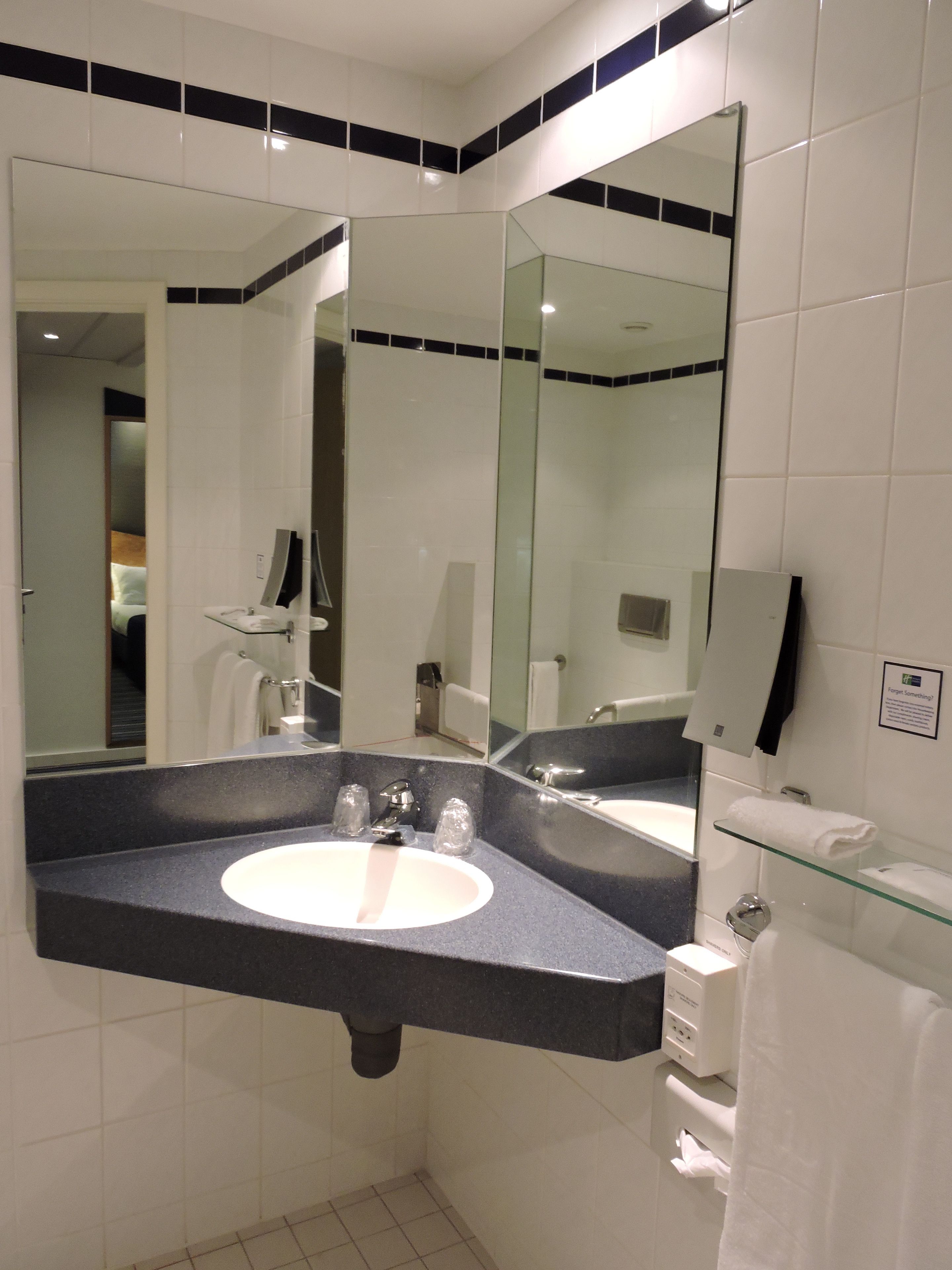 Een moderne badkamer met een grote spiegel, een wit wastafelmeubel en een glazen plank.