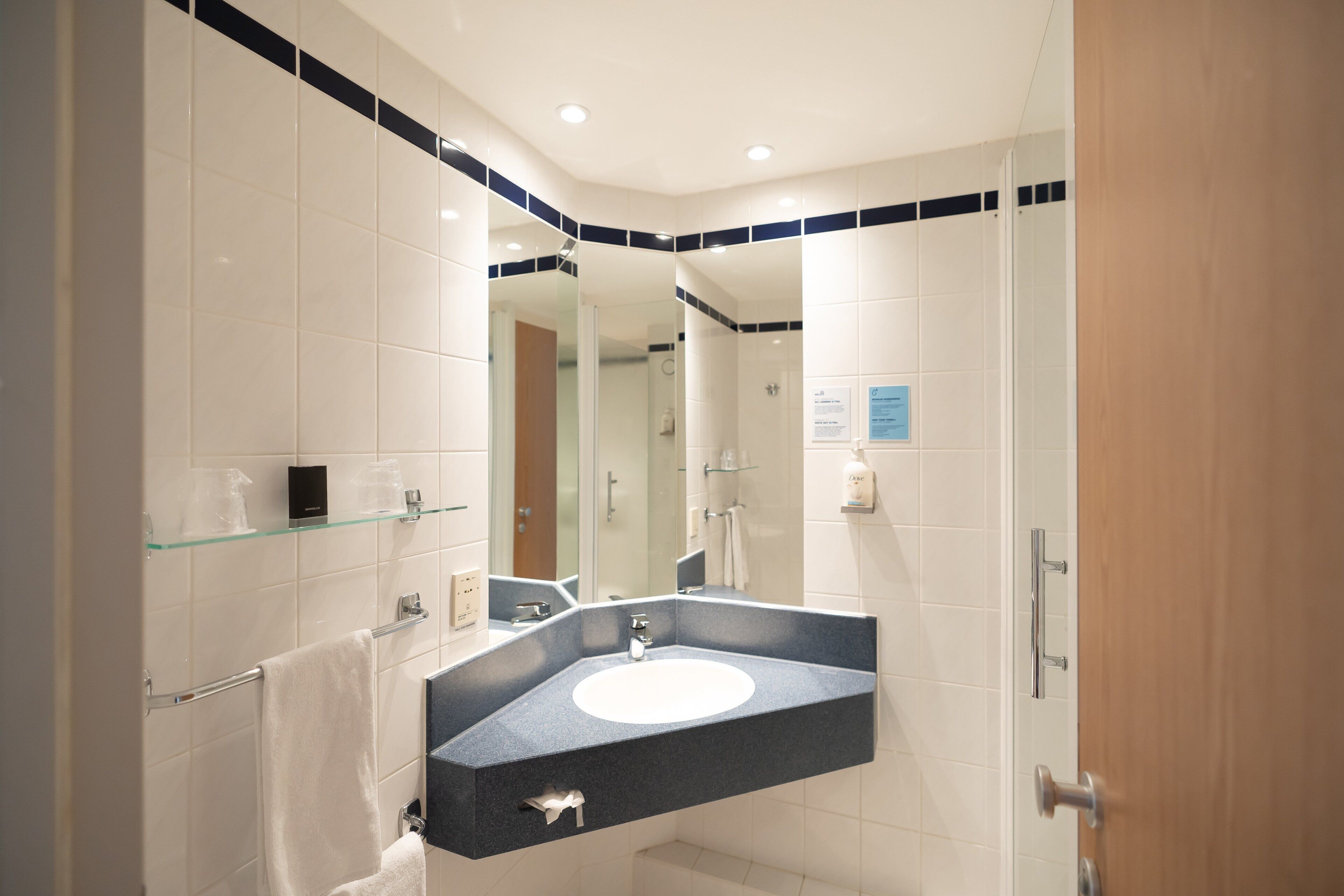 A modern bathroom with a curved sink, glass shelves, and a shower area.