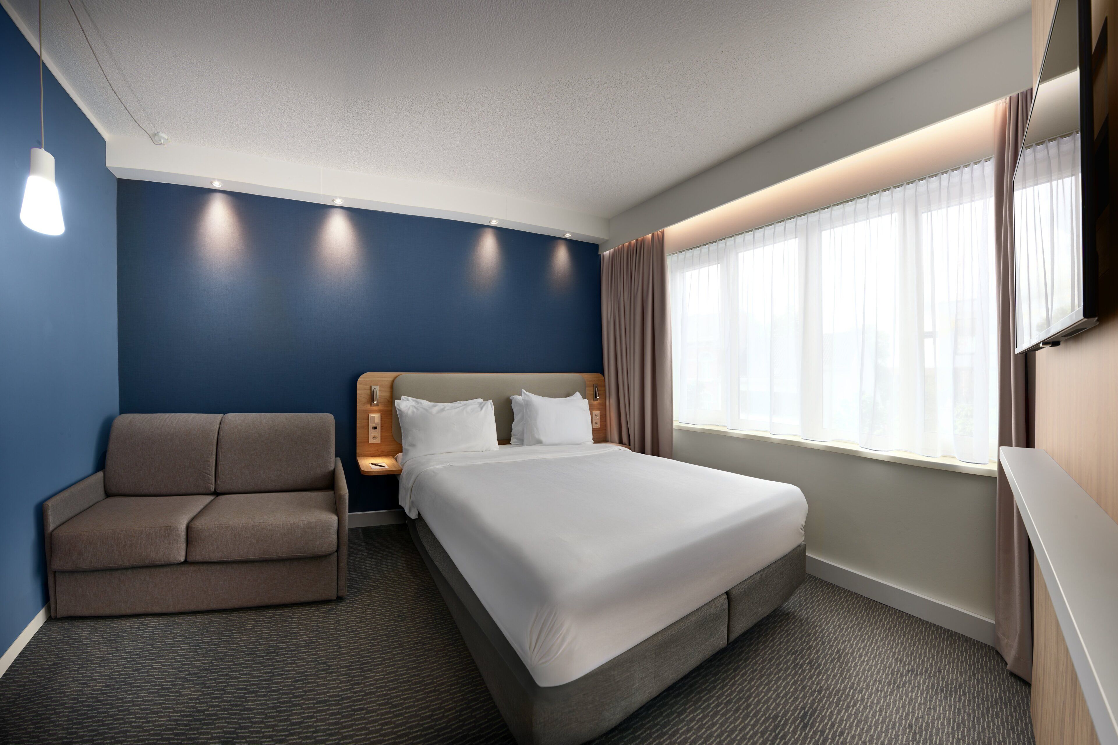 Una habitación de hotel con una cama, un sofá, una mesita de noche y un televisor.