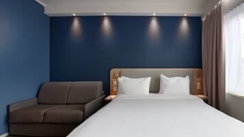 A hotel room with a bed, a sofa, a nightstand, and a window with curtains.