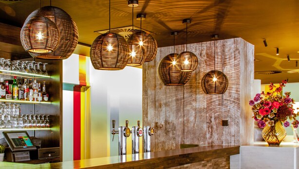A modern bar area with a wooden bar counter, multiple stools, and hanging pendant lights. - Holiday Inn Express Hasselt by IHG (Hasselt)