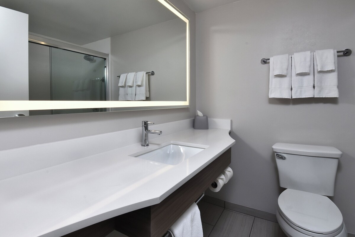 A modern bathroom with a large mirror, two sinks, a toilet, and a towel rack with three towels.